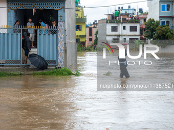 A man is attempting to cross a flooded road with his belongings packed in a suitcase in Tikathali, Kathmandu, on July 6, 2024, following inc...