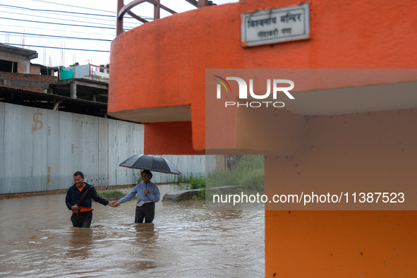 A man is helping a girl cross the flooded road in Tikathali, Kathmandu, on July 6, 2024, following incessant rainfall. 