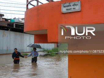 A man is helping a girl cross the flooded road in Tikathali, Kathmandu, on July 6, 2024, following incessant rainfall. (