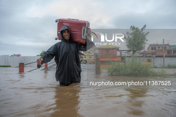 A man is attempting to cross a flooded road with his belongings packed in a suitcase in Tikathali, Kathmandu, on July 6, 2024, following inc...