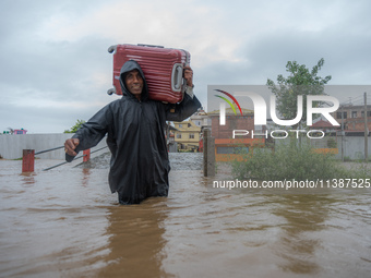 A man is attempting to cross a flooded road with his belongings packed in a suitcase in Tikathali, Kathmandu, on July 6, 2024, following inc...