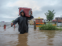 A man is attempting to cross a flooded road with his belongings packed in a suitcase in Tikathali, Kathmandu, on July 6, 2024, following inc...