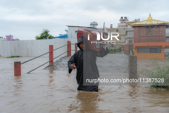 A man is attempting to cross a flooded road with his belongings packed in a suitcase in Tikathali, Kathmandu, on July 6, 2024, following inc...