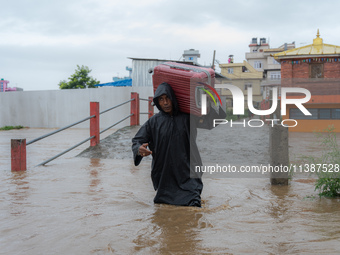 A man is attempting to cross a flooded road with his belongings packed in a suitcase in Tikathali, Kathmandu, on July 6, 2024, following inc...