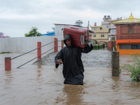 A man is attempting to cross a flooded road with his belongings packed in a suitcase in Tikathali, Kathmandu, on July 6, 2024, following inc...