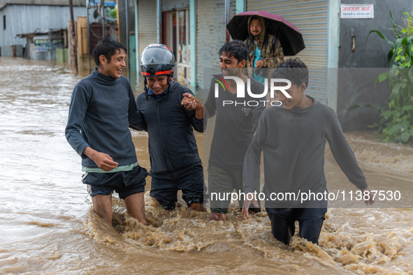 People are crossing the flooded road in Tikathali, Kathmandu, on July 06, 2024, following incessant rainfall 