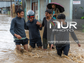 People are crossing the flooded road in Tikathali, Kathmandu, on July 06, 2024, following incessant rainfall (