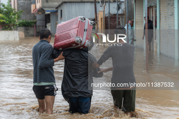 Two young boys are helping a man cross a flooded road with a suitcase in Tikathali, Kathmandu, on July 6, 2024, after incessant rainfall. 