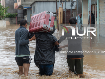 Two young boys are helping a man cross a flooded road with a suitcase in Tikathali, Kathmandu, on July 6, 2024, after incessant rainfall. (