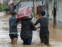 Two young boys are helping a man cross a flooded road with a suitcase in Tikathali, Kathmandu, on July 6, 2024, after incessant rainfall. (