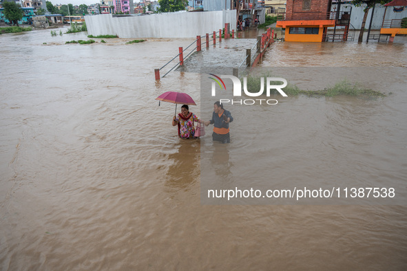 A man is helping a girl cross the flooded road in Tikathali, Kathmandu, on July 6, 2024, following incessant rainfall. 