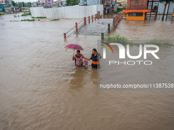 A man is helping a girl cross the flooded road in Tikathali, Kathmandu, on July 6, 2024, following incessant rainfall. (