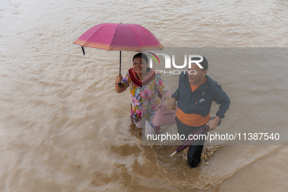 A man is helping a girl cross the flooded road in Tikathali, Kathmandu, on July 6, 2024, following incessant rainfall. 