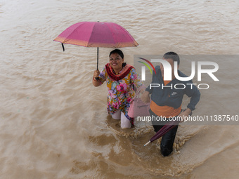 A man is helping a girl cross the flooded road in Tikathali, Kathmandu, on July 6, 2024, following incessant rainfall. (