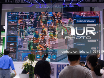 Visitors are being seen in front of a large screen of the security system at the World Artificial Intelligence Conference at the Shanghai Wo...