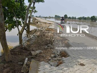 A man is riding a bike on a road damaged by flood in Nagaon District of Assam, India, on July 7, 2024. (