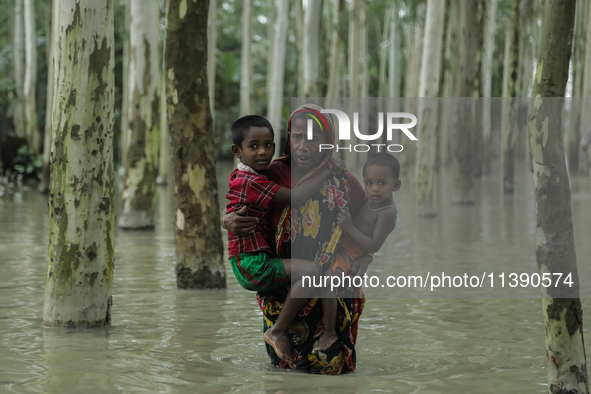 A woman is paddling through flooded water while carrying her children in Kurigram, Bangladesh, on July 7, 2024. 