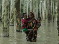 A woman is paddling through flooded water while carrying her children in Kurigram, Bangladesh, on July 7, 2024. (