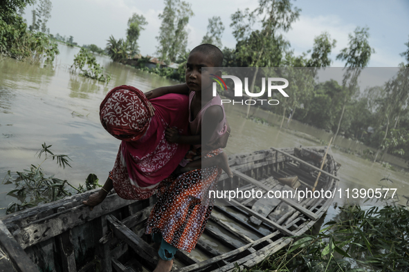 A woman is migrating locally with her daughter to high land as their home is submerged by flood water in Kurigram, Bangladesh, on July 7, 20...