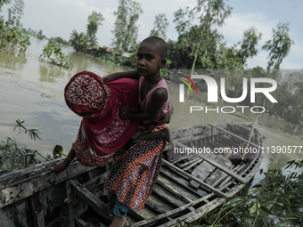 A woman is migrating locally with her daughter to high land as their home is submerged by flood water in Kurigram, Bangladesh, on July 7, 20...