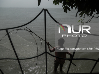 A boy is trying to catch fish from his washed-off house due to flood water in Kurigram, Bangladesh, on July 8, 2024. (