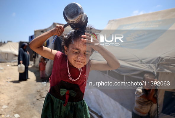 A displaced Palestinian girl is splashing her face with water in front of her tent during a heatwave in Deir al-Balah, in the central Gaza S...