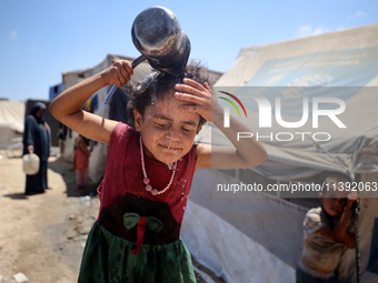 A displaced Palestinian girl is splashing her face with water in front of her tent during a heatwave in Deir al-Balah, in the central Gaza S...