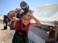 A displaced Palestinian girl is splashing her face with water in front of her tent during a heatwave in Deir al-Balah, in the central Gaza S...