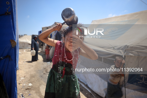 A displaced Palestinian girl is splashing her face with water in front of her tent during a heatwave in Deir al-Balah, in the central Gaza S...