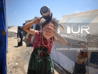 A displaced Palestinian girl is splashing her face with water in front of her tent during a heatwave in Deir al-Balah, in the central Gaza S...