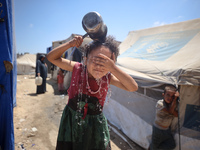 A displaced Palestinian girl is splashing her face with water in front of her tent during a heatwave in Deir al-Balah, in the central Gaza S...