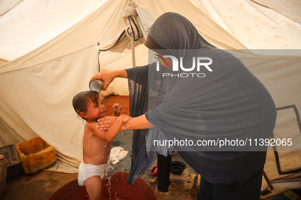 A Palestinian woman is washing a child in front of her tent during a heatwave in Deir al-Balah, in the central Gaza Strip, on July 8, 2024,...