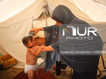 A Palestinian woman is washing a child in front of her tent during a heatwave in Deir al-Balah, in the central Gaza Strip, on July 8, 2024,...