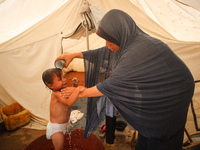 A Palestinian woman is washing a child in front of her tent during a heatwave in Deir al-Balah, in the central Gaza Strip, on July 8, 2024,...