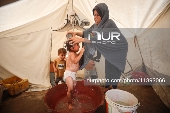 A Palestinian woman is washing a child in front of her tent during a heatwave in Deir al-Balah, in the central Gaza Strip, on July 8, 2024,...