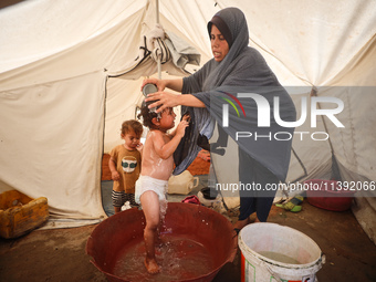 A Palestinian woman is washing a child in front of her tent during a heatwave in Deir al-Balah, in the central Gaza Strip, on July 8, 2024,...