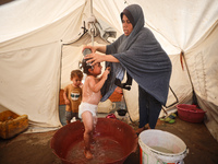 A Palestinian woman is washing a child in front of her tent during a heatwave in Deir al-Balah, in the central Gaza Strip, on July 8, 2024,...