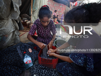 Displaced Palestinian girls are hand-washing clothes with a bar of soap at their displacement tent in Deir el-Balah in the central Gaza Stri...