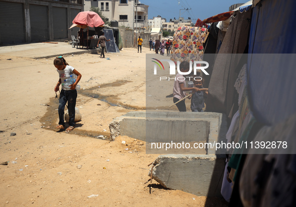 A girl is pulling a cart of water containers past a line of displacement tents in Deir el-Balah, Gaza Strip, on July 8, 2024, amid the ongoi...