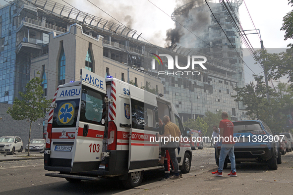 An ambulance is parking near the Lukianivska metro station as smoke is rising over an unfinished building during a Russian missile attack in...