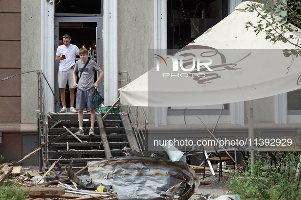 Two men are sitting on steps outside a coffee shop near the Lukianivska metro station damaged during a Russian missile attack in Kyiv, Ukrai...