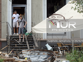 Two men are sitting on steps outside a coffee shop near the Lukianivska metro station damaged during a Russian missile attack in Kyiv, Ukrai...