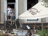 Two men are sitting on steps outside a coffee shop near the Lukianivska metro station damaged during a Russian missile attack in Kyiv, Ukrai...