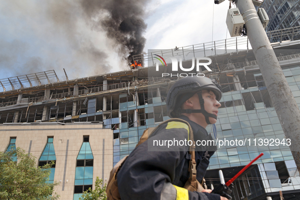 A rescue worker is walking past as a pillar of smoke is rising from the burning roof of an unfinished building near the Lukianivska metro st...