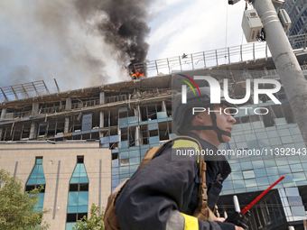 A rescue worker is walking past as a pillar of smoke is rising from the burning roof of an unfinished building near the Lukianivska metro st...