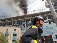 A rescue worker is walking past as a pillar of smoke is rising from the burning roof of an unfinished building near the Lukianivska metro st...