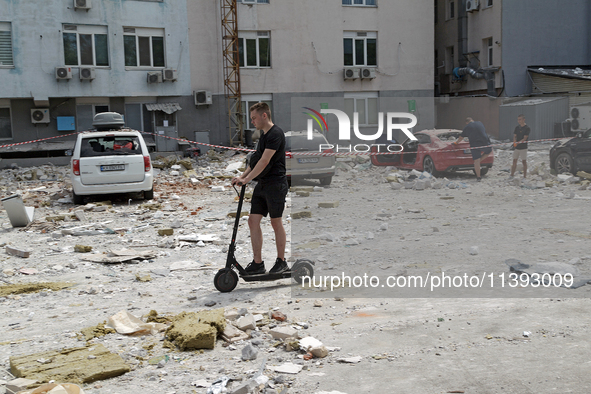 A man is riding an electric scooter past an office building damaged by a Russian missile strike in the Solomianskyi district in Kyiv, Ukrain...