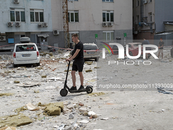 A man is riding an electric scooter past an office building damaged by a Russian missile strike in the Solomianskyi district in Kyiv, Ukrain...