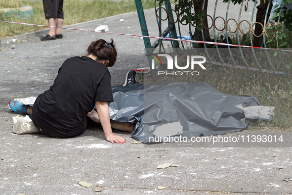 A woman is sitting on the ground by a man killed by a Russian missile strike in the Solomianskyi district in Kyiv, Ukraine, on July 8, 2024....