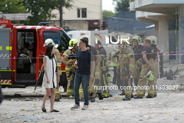 A man and woman are standing before rescue workers during a response effort to a Russian missile strike in the Solomianskyi district in Kyiv...